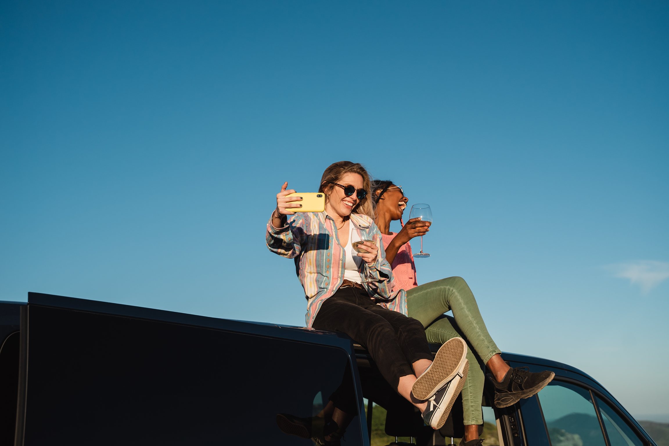 Two women laughing on top of a car