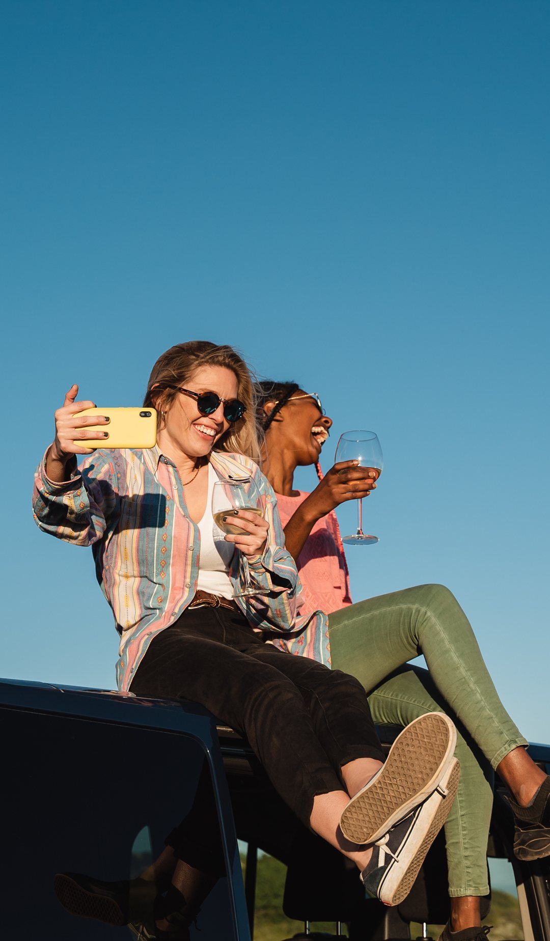 Two women laughing on top of a car